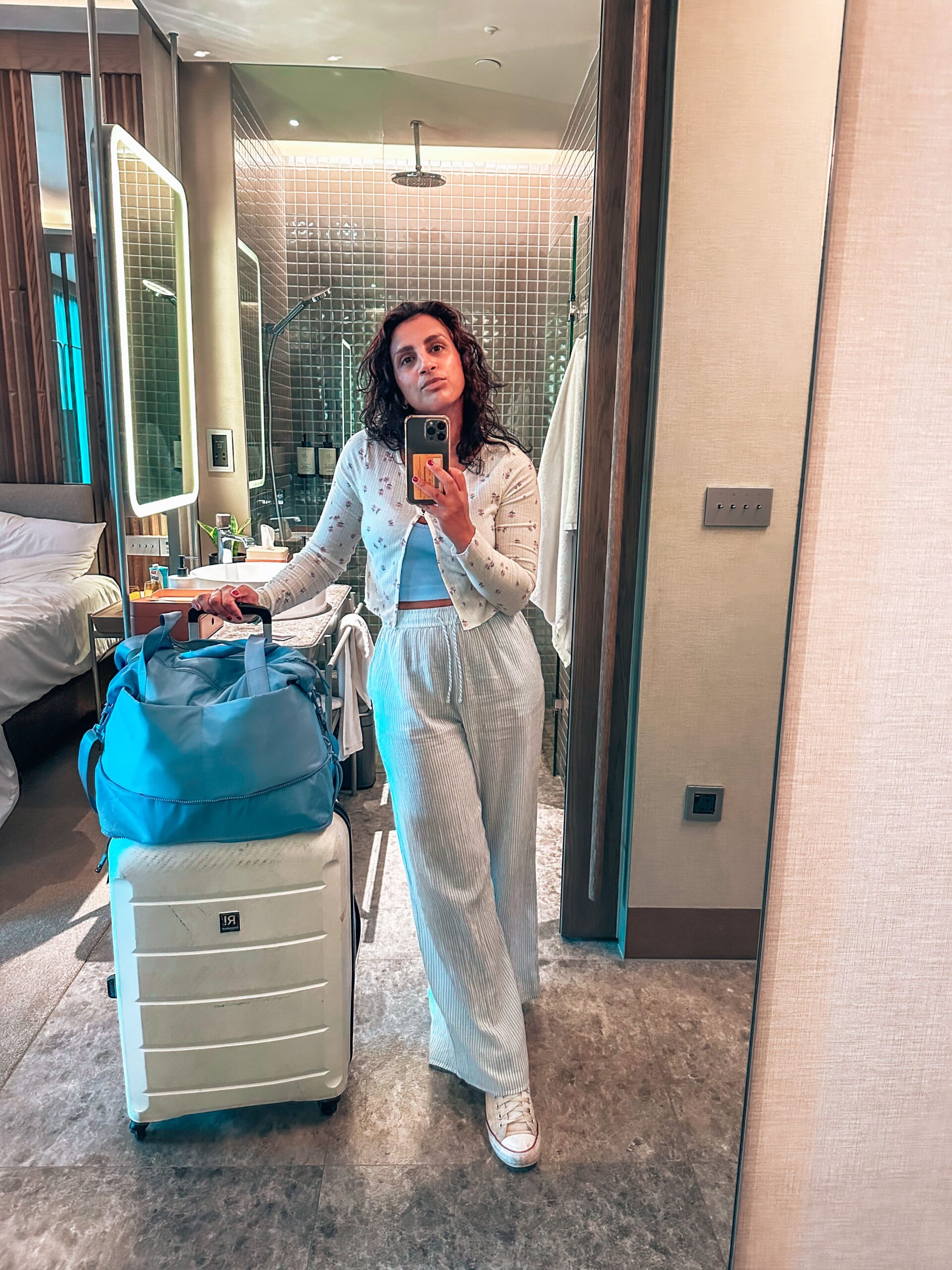 Solo travel girl takes mirror selfie with suitcase and bag packed for the airport in hotel room - 14 Solo Travel Hacks to Survive Early Morning Flights